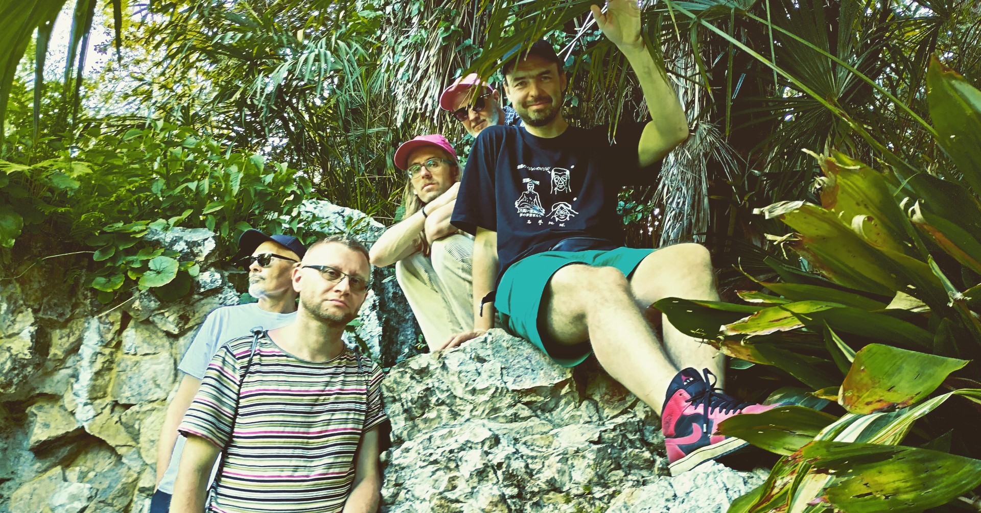 The photo shows five men surrounded by green, exotic plants.