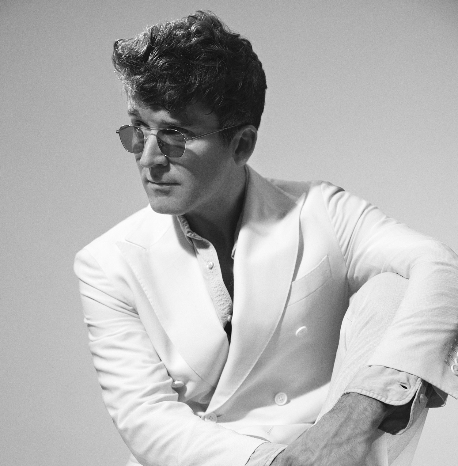 The photo shows a seated man wearing sunglasses and a suit.