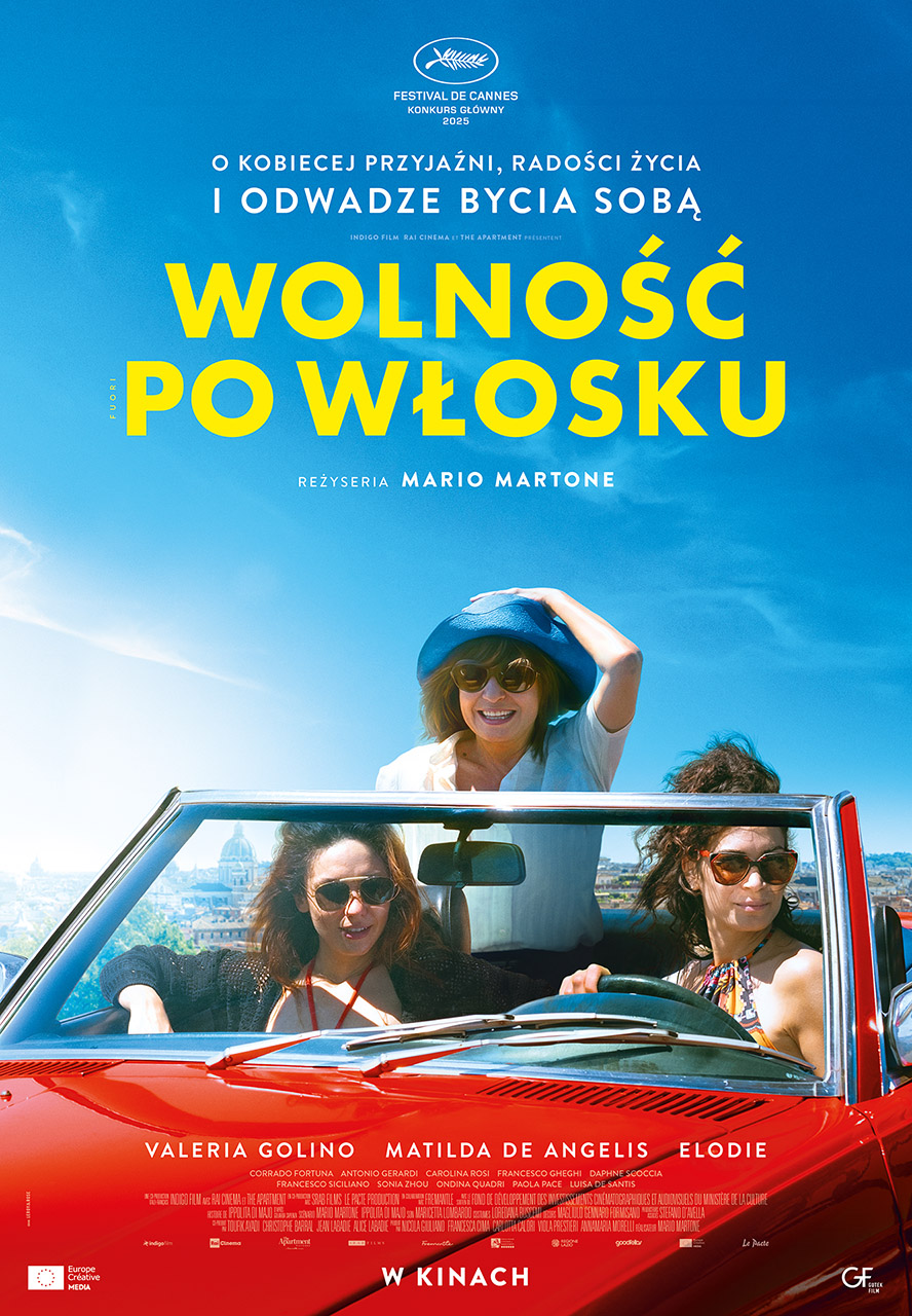trzy kobiety w czerwonym kabriolecie, jedna siedzi wyżej i trzyma kapelusz. w tle błękitne niebo.