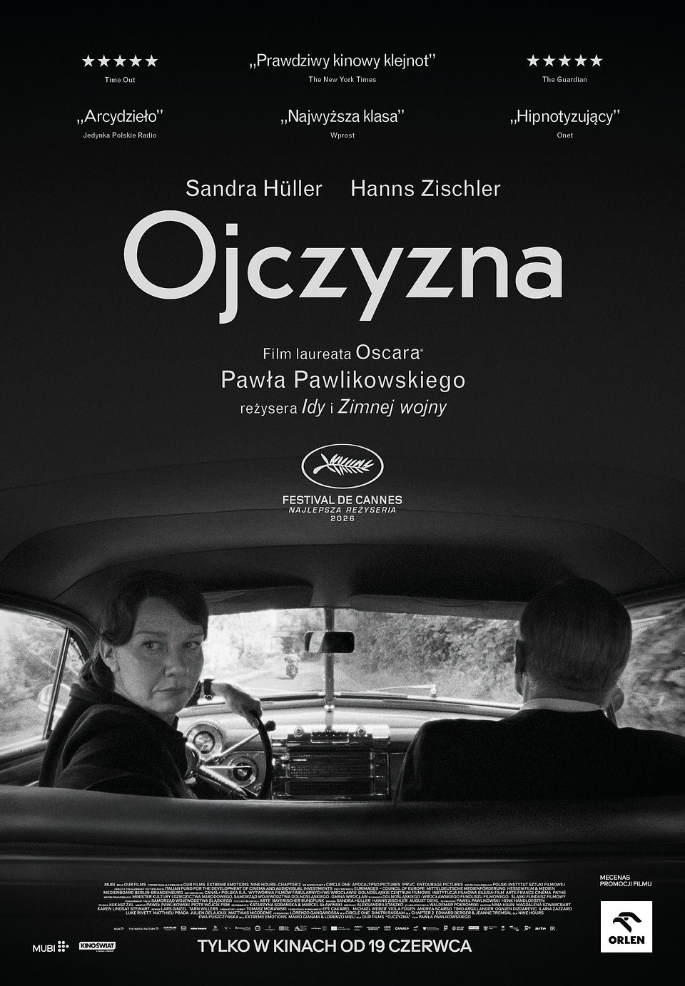 Czarno-biały plakat filmowy filmu „Ojczyzna” w reżyserii Pawła Pawlikowskiego. Na dole kadru wnętrze starego samochodu widziane z tylnego siedzenia. Kobieta prowadząca auto odwraca głowę w stronę widza, obok siedzi mężczyzna pokazany od tyłu. Nad nimi duży biały tytuł „Ojczyzna”, a wyżej nazwiska aktorów Sandry Hüller i Hannsa Zischlera. U góry znajdują się cytaty recenzji i oceny gwiazdkowe. Plakat utrzymany jest w minimalistycznej, mrocznej estetyce, z dominacją czerni i szarości. Na dole informacja o nagrodzie za reżyserię w Cannes oraz data premiery kinowej: „Tylko w kinach od 19 czerwca”. Bo przecież współczesne kino artystyczne nie może obyć się bez czerni, ciszy i ludzi patrzących przez ramię z egzystencjalnym niepokojem.