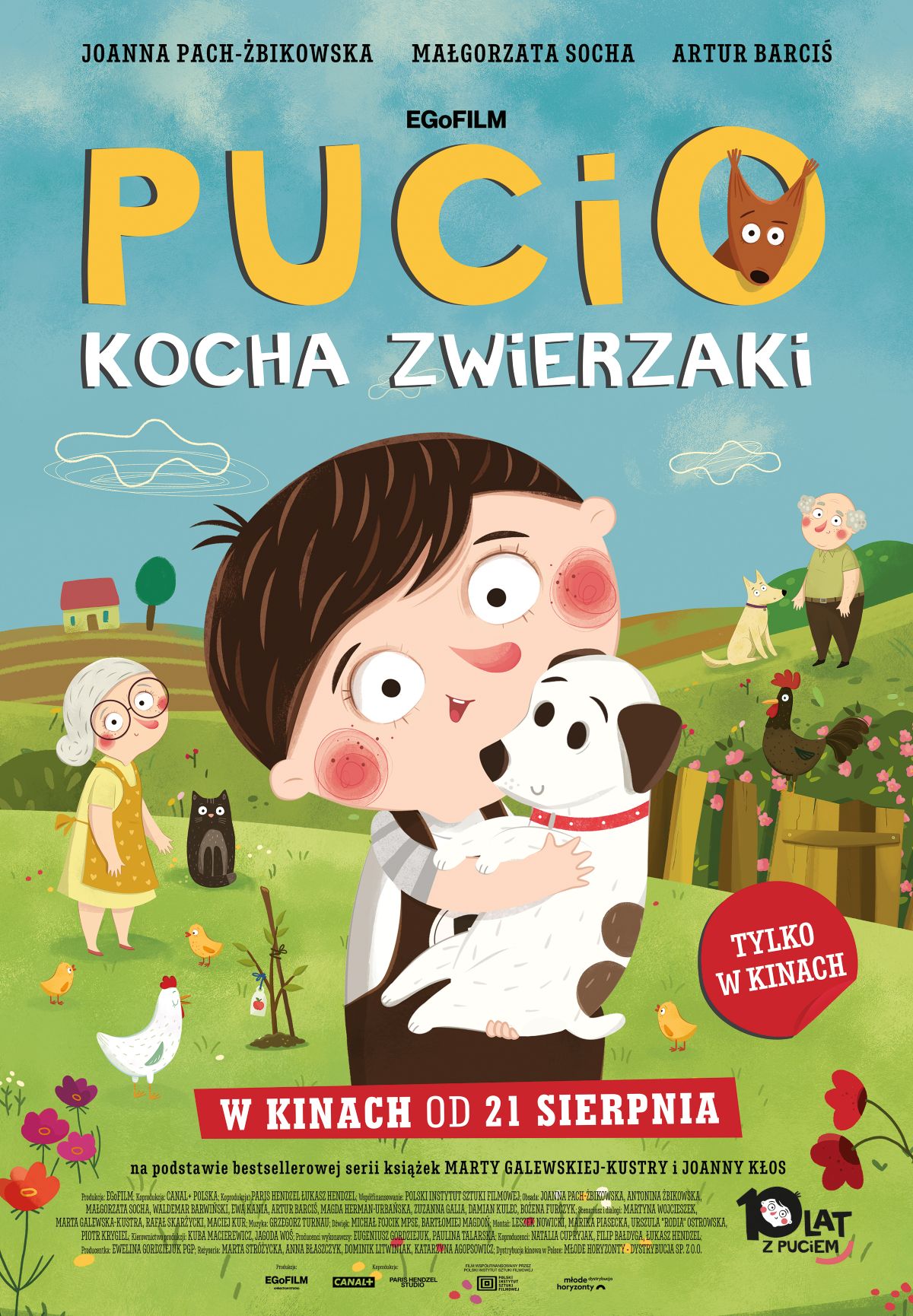 chłopiec tuli czarno-białego łaciatego szczeniaka, w tle babcia, trawnik i płot.