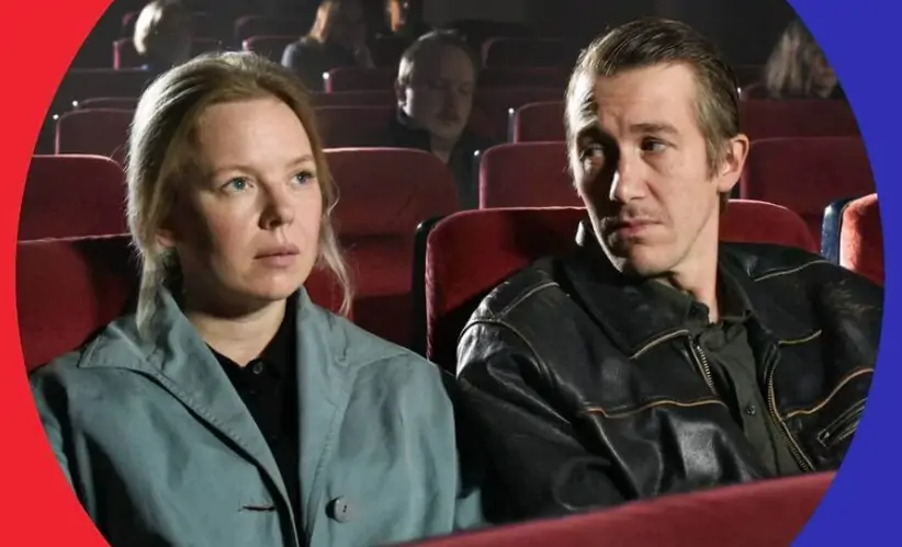 Kadr z filmu "Opadające liście". Zdjęcie przedstawia kobietę i mężczyznę siedzących na sali kinowej w czerwonych, skórzanych fotelach. Kobieta o blond włosach jest ubrana w zielony płaszcz i czarną bluzkę. Mężczyzna ma na sobie czarną, skórzaną kurtkę.