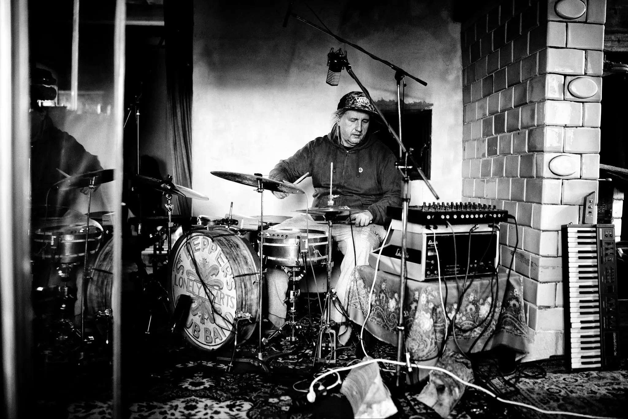 The photo shows a long-haired man sitting behind a drum kit.