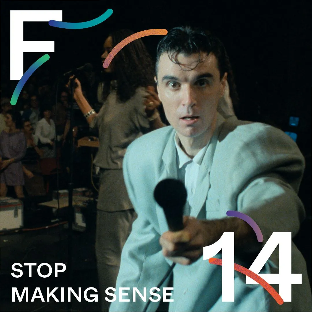 mężczyzna - brunet - w jasnym garniturze, wyciąga mikrofon w stronę widza.